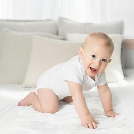 Zweisilbige Jungennamen sind bei Eltern sehr beliebt. Ein kleiner Junge kniet auf dem Bett.