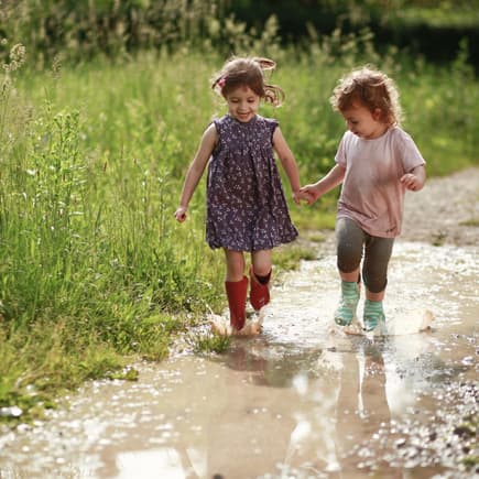 Kinder lieben die Natur – und Eltern können diese Begeisterung unterstützen. Zwei Kinder laufen durch eine Pfütze.