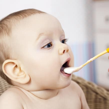 Anzeichen verraten, ob das Baby schon reif für Beikost ist. Baby isst Brei.