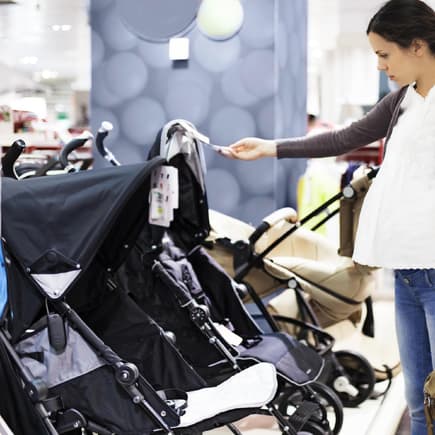 Den richtigen Kinderwagen zu finden, ist bei der großen Auswahl gar nicht so einfach. Eine Mutter mit Babybauch steht im Geschäft und schaut sich Kinderwagen an.