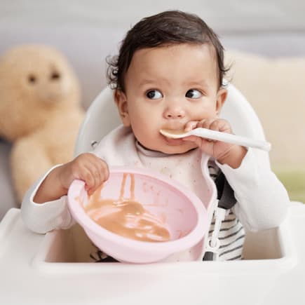 Obstbrei für Babys im Test. Baby löffelt Obstbrei.