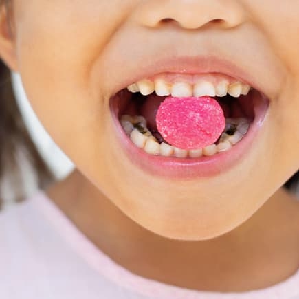 Keine Überraschung: Süßigkeiten fördern Karies. Ein Mädchen mit Bonbon zwischen den Zähnen.