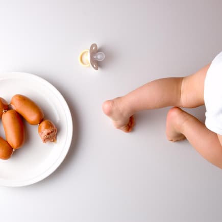 Wüstchen sind kein geeignetes Lebensmittel für Babys. Baby krabbelt weg von einem Würstchenteller.