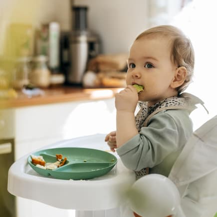 Müsliriegel für Babys wegen Schimmel zurückgerufen. Baby isst im Hochstuhl.