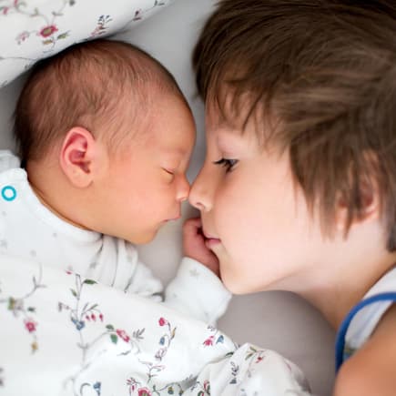 Geschwisterkonstellationen haben einen Einfluss auf unsere Entwicklung. Großer Bruder liegt neben Baby im Bett.