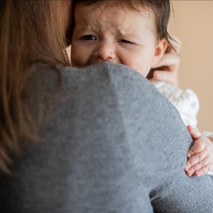 Fremdeln ist eine ganz normale Verhaltensweise. Baby weint auf Mamas Arm.