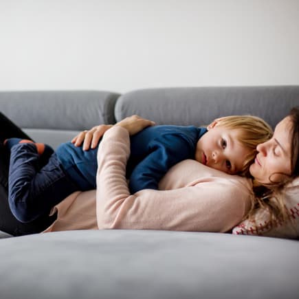 Wenn Kinder krank sind, wirkt Kuscheln Wunder. Mutter hält krankes Kind, liegen zusammen auf einer Couch.