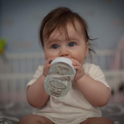 Trinklernbecher werden meist ab etwa 6 Monaten empfohlen. Baby trinkt aus Trinklernbecher.
