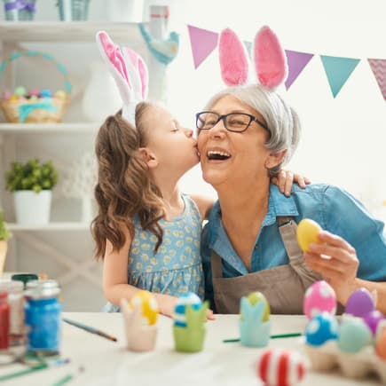 Osterwünsche und Sprüche freuen Kinder und Erwachsene. Enkeltochter gibt Oma einen Kuss, beide tragen Hasenohren.