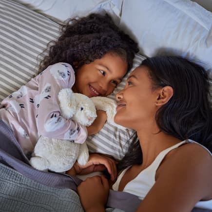Eine Abendroutine gibt Kindern Geborgenheit. Mama und Tochter liegen im Bett.