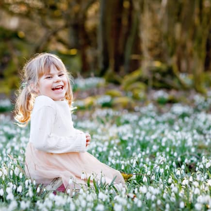 Frühblüher wie Schneeglöcken können giftig sein. Kleines Mädchen sitzt in Schneeglöckchen.