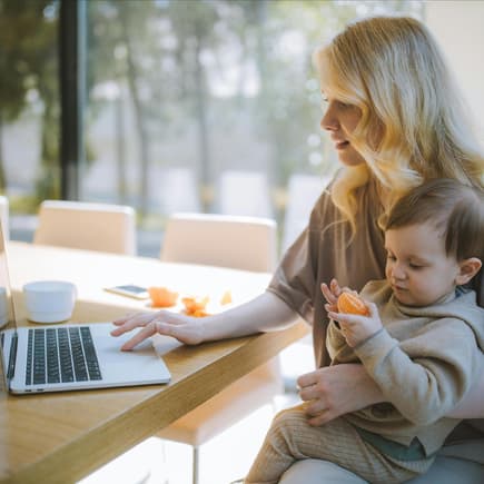 Berufstätige Mütter verfügen oft über starke Soft Skills. Eine Mutter sitzt am Computer und hat ihren kleinen Sohn auf dem Schoß.