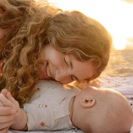 Im Sommer reicht luftige Kleidung fürs Baby. Glückliche Mutter legt am Strand ihren Kopf aufs Baby.