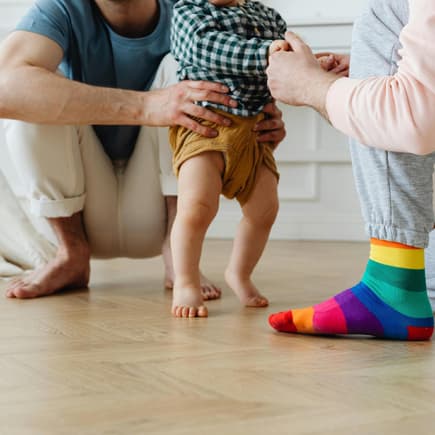 Barfuß ist am besten – vor allem zum Start. Baby läuft barfuß mit Hilfe von einem zum anderen.
