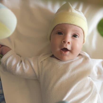 Dein Baby wird von deinem selbst gebastelten Mobile ganz begeistert sein. Baby liegt fröhlich unter einem Mobile.