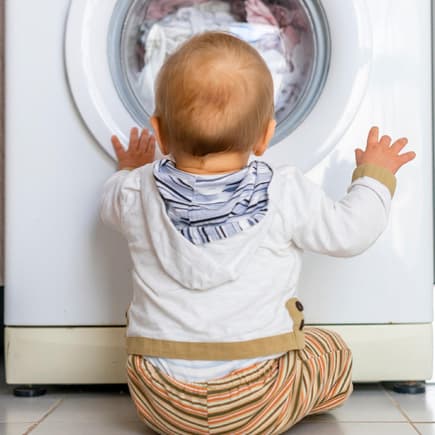 So eine Waschmaschine ist nicht nur praktisch, sondern für Babys auch ganz schön faszinierend. Baby sitzt vor der Waschmaschine und schaut hinein.