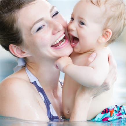 In Schwimmbädern sind Schwimmwindeln für Babys Pflicht. Ein Baby in Schwimmwindeln plantscht mit seiner Mutter im Schwimmbad.