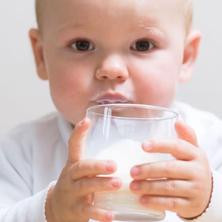 Eltern sollten einige Dinge beachten, wenn sie ihrem Baby Kuhmilch geben. Kleinkind trinkt Milch aus dem Glas.
