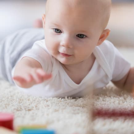 PEKiP-Übungen sollen das Baby in seiner Entwicklung begleiten und fördern. Baby greift nach Bausteinen.