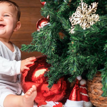 Genau so soll es an Weihnachten sein: Das Baby lacht vergnügt unterm geschmückten Baum.