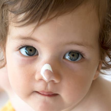 Eltern wollen immer das Beste für ihr Kind – das gilt auch für Pflegeprodukte. Kleinkind mit Cremetupfer auf der Nase.