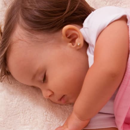 Viele Eltern lassen ihren Kindern bereits im Babyalter Ohrlöcher stechen. Schlafendes Baby mit Ohrring.