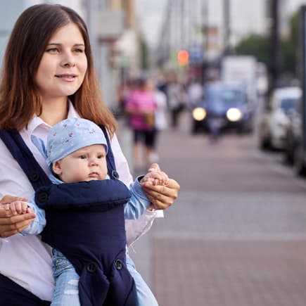 Viele Eltern fragen sich, ob es schädlich ist, dass Baby in der Trage nach vorne schauen zu lassen. Eine Mutter trägt ihr Baby mit Blick nach vorne in der Trage