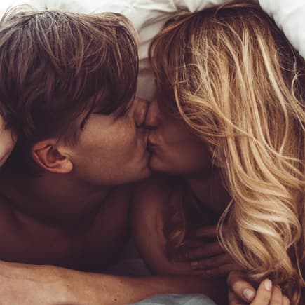 Wer schwanger werden will, sollte wissen zu welcher Tageszeit der Eisprung stattfindet. Ein Paar, das sich im Bett küsst.