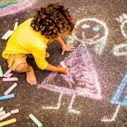 Mit selbst gemachter Kreide können eure Kinder den Asphalt verschönern. Kind malt mit Straßenmalkreide.