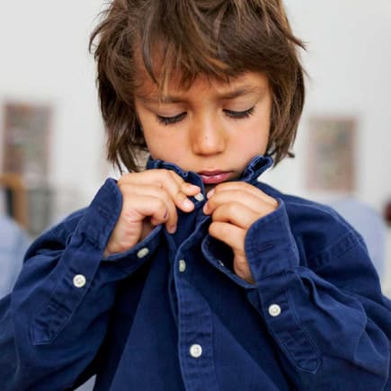 Wer kennt's? Knöpfe können für kleine Kinder der Endgegner sein. Junge versucht, sein Hemd zuzuknöpfen.