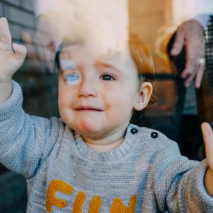Fremdbetreuung in der Kita kann für kleine Kinder tatsächlich schädlich sein. Kleinkind hinter der Scheibe weint beim Abschied.