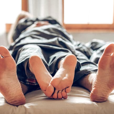 Für manche Eltern fällt der Weg zurück zur intimen Zärtlichkeit schwer. Paar liegt unter dem Laken aufeinander, die Füße schauen heraus.