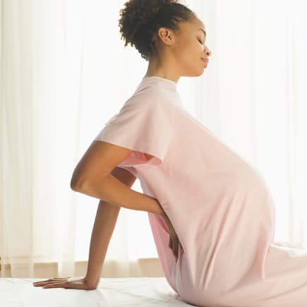 Es gibt einige Methoden, mit denen man Wehen fördern kann. Eine schwangere Frau hält sich mit einer Hand den schmerzenden Rücken.