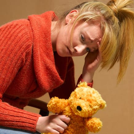 Bei einer postpartalen Depression erscheint alles schwer. Erschöpfte, mutlose Frau mit Teddy in der Hand.