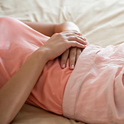 Stellt euch vor, ihr seid schwanger und merkt es nicht! Unbemerkte Schwangerschaften kommen tatsächlich ab und an vor! Frau liegt auf dem Bett und hält sich die Hände auf den Bauch.