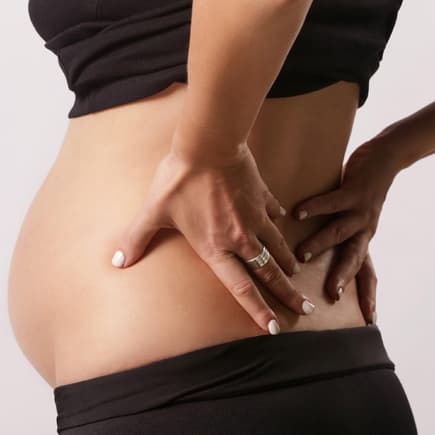 Fast keine Frau bleibt von Rückenschmerzen in der Schwangerschaft verschont. Schwangere Frau hält sich den Rücken.