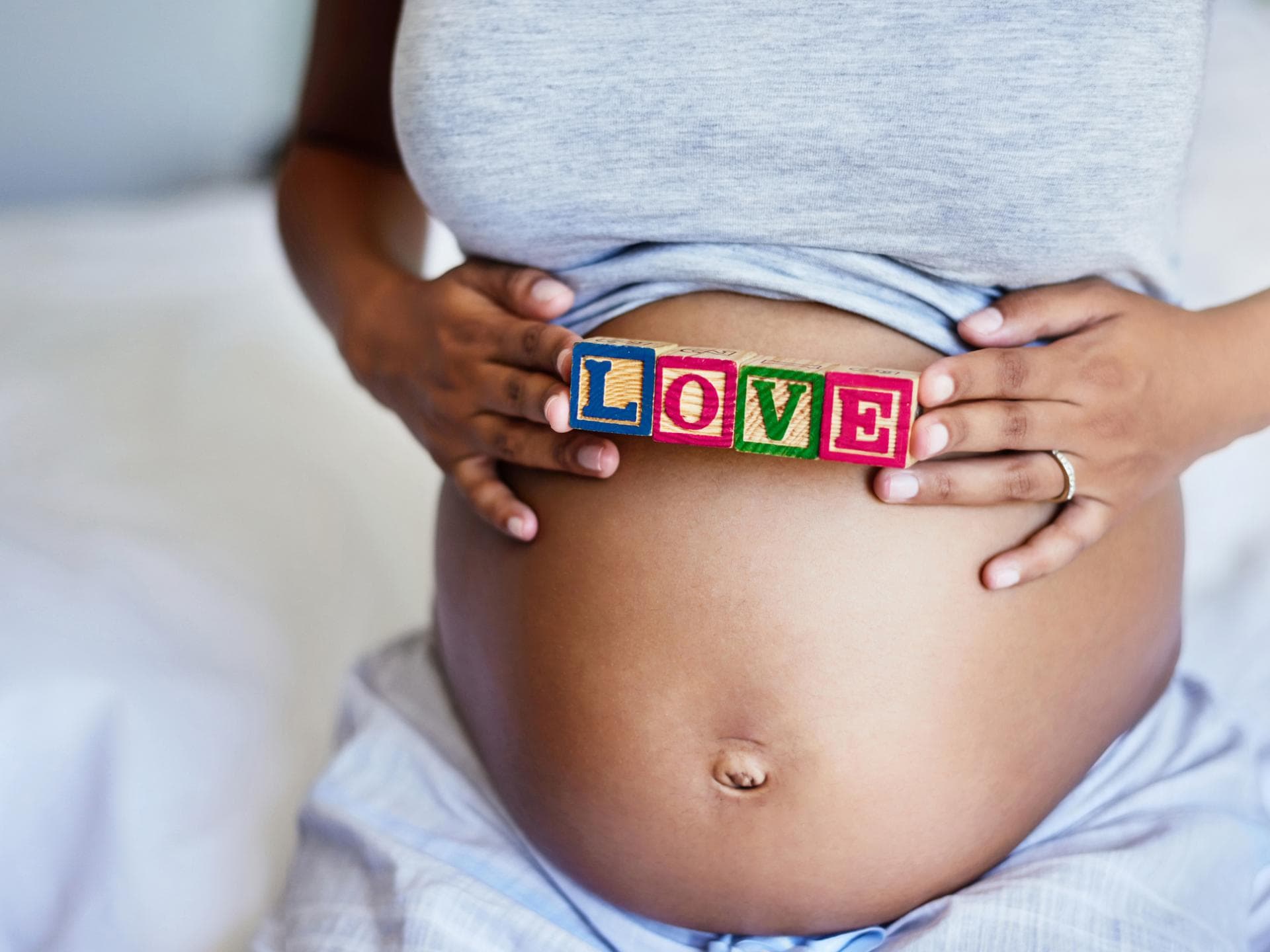 Mit dem wachsenden Babybauch verändert sich auch der Bauchnabel in der Schwangerschaft. Eine Mama hält ein Love-Schild über ihren kugelrunden Babybauch.