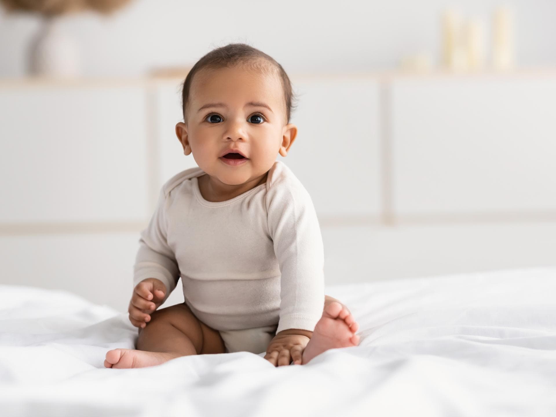 Von Baptist bis Brandon: Hier kommen die schönsten Jungennamen mit B. Ein kleiner Junge sitzt fröhlich auf dem Bett.