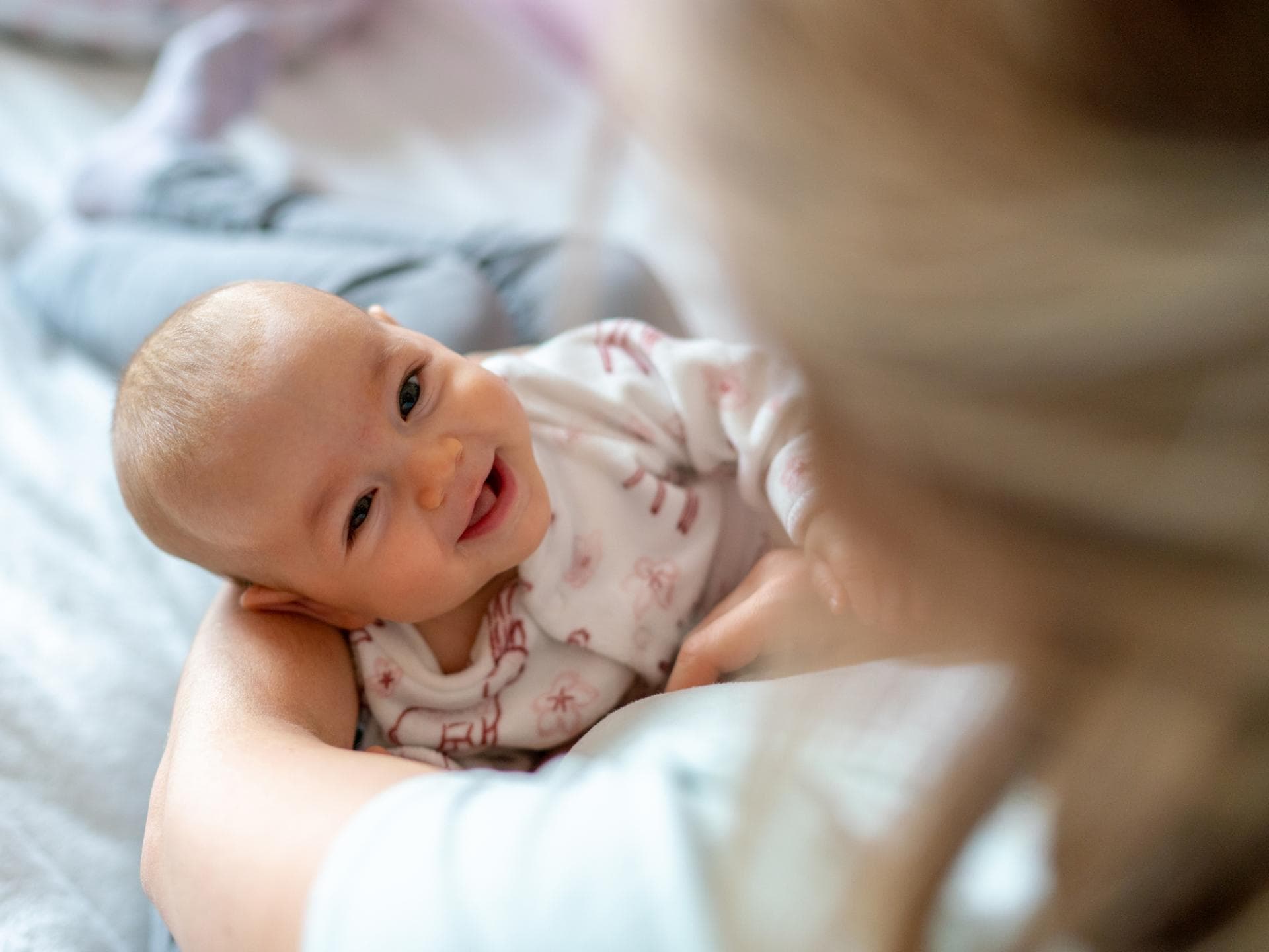 Hier findet ihr seltene Mädchennamen mit dem Buchstaben Q. Ein Baby liegt lachend in Mamas Armen.