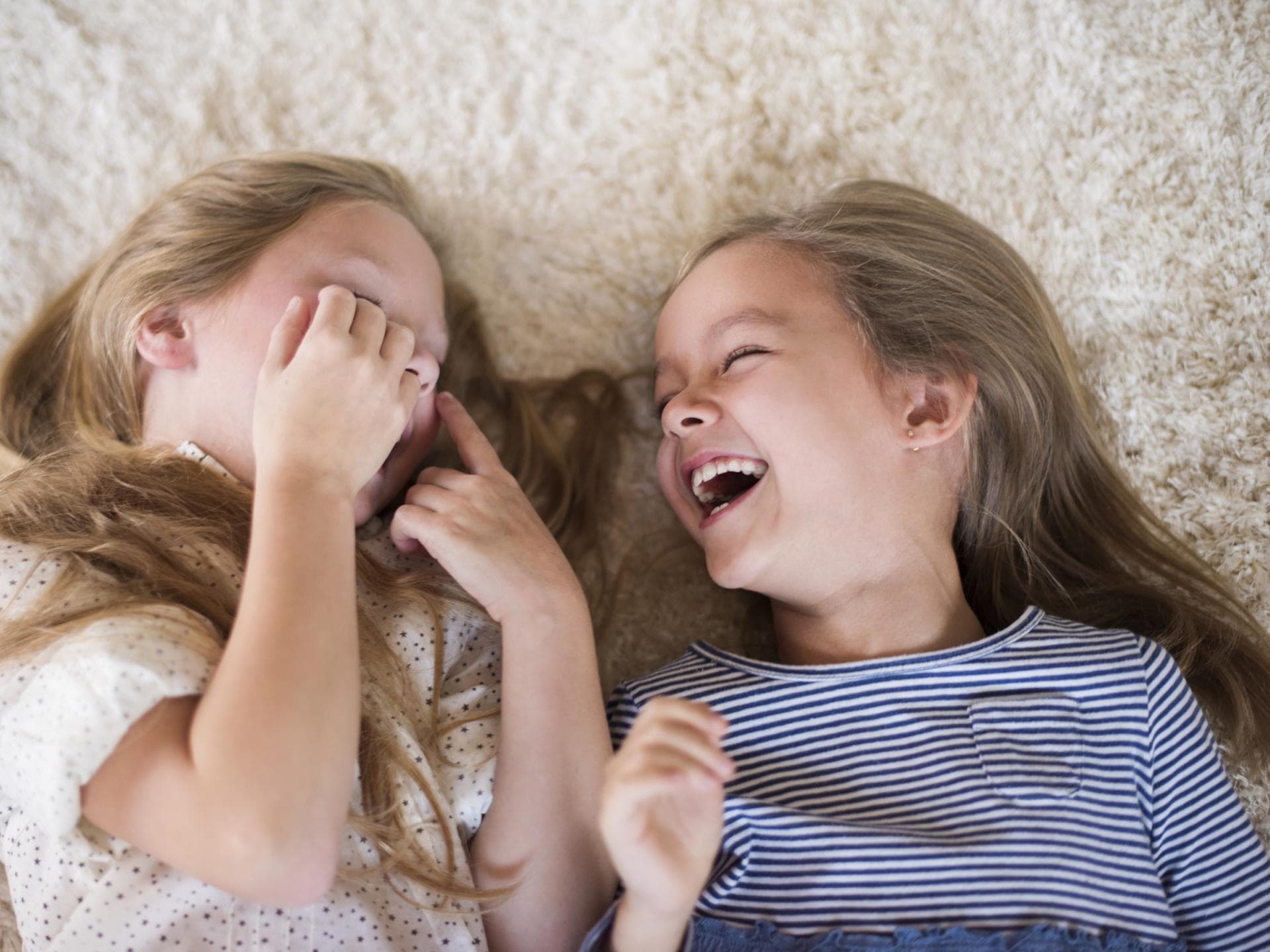 "Alle Kinder Witze" sind oft ganz schön gemein, aber auch sehr lustig. Zwei Mädchen liegen lachend auf dem Boden.