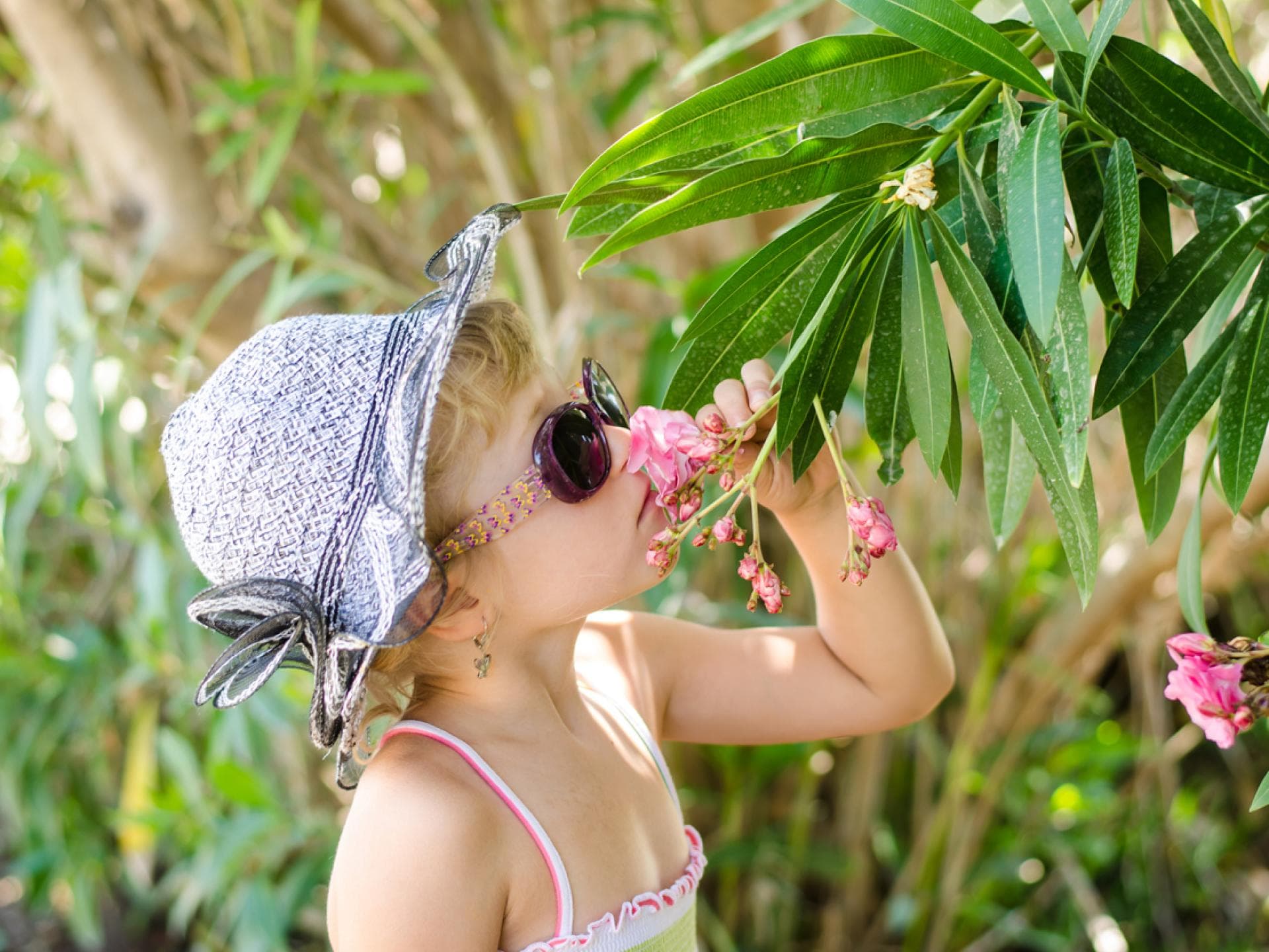 Mädchen mit Hut und Sonnenbrille riecht an einem Blumenstrauch im Garten Mädchen mit Hut und Sonnenbrille riecht an einem Blumenstrauch im Garten