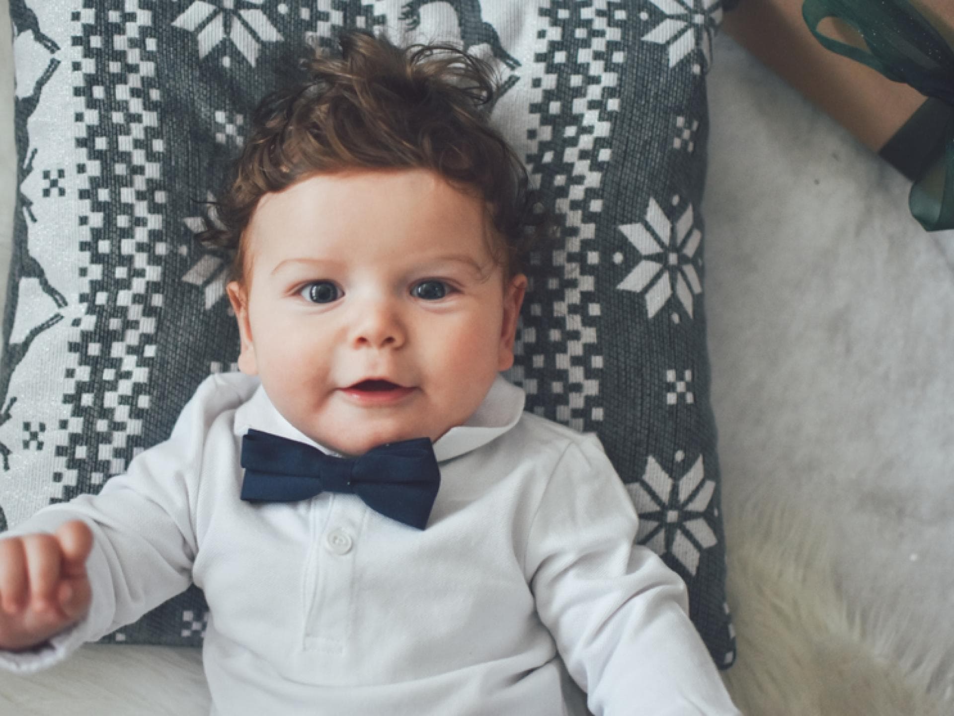 Kleiner Junge mit Fliege lächelt auf einem Kissen liegend in die Kamera. Kleiner Junge mit Fliege lächelt auf einem Kissen liegend in die Kamera.