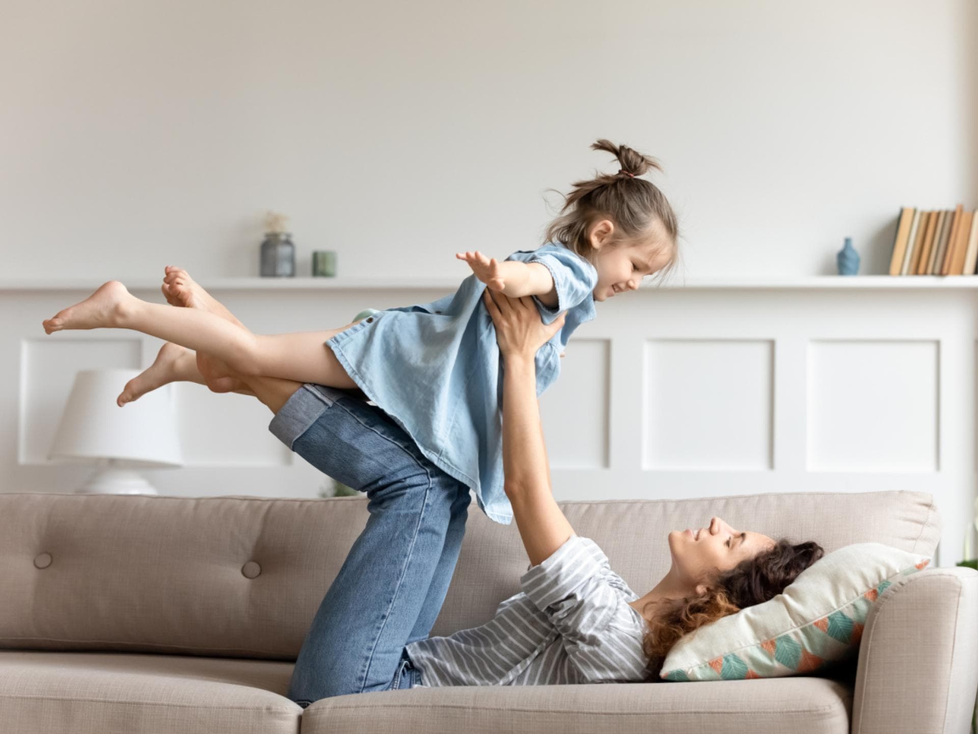 Mütter haben nach einer Scheidung finanziell oft das Nachsehen. Mutter liegt auf der Couch und hebt ihre Tochter hoch.