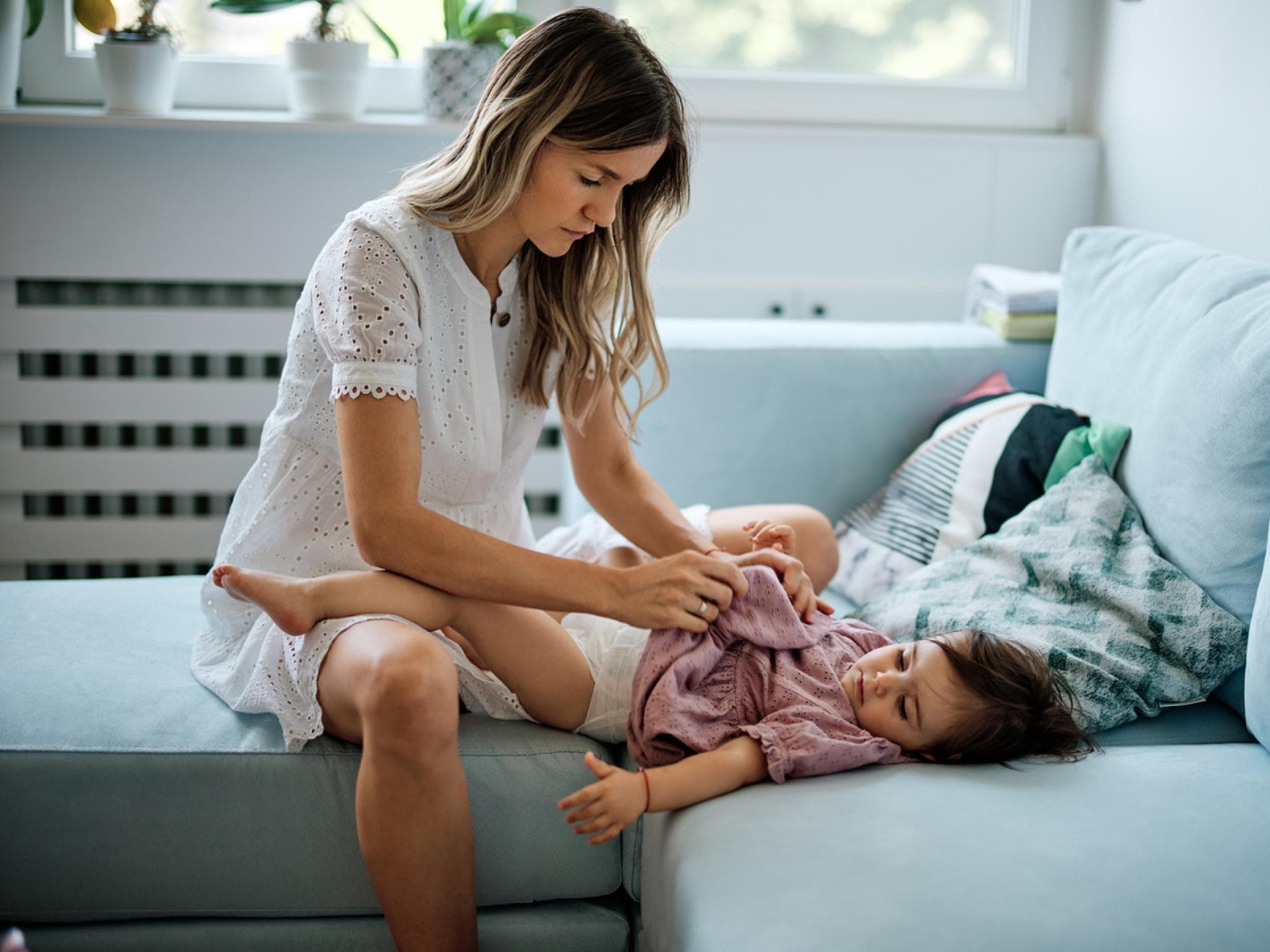 Junge Mutter wickelt ihre kleine Tochter auf dem Sofa. Junge Mutter wickelt ihre kleine Tochter auf dem Sofa.