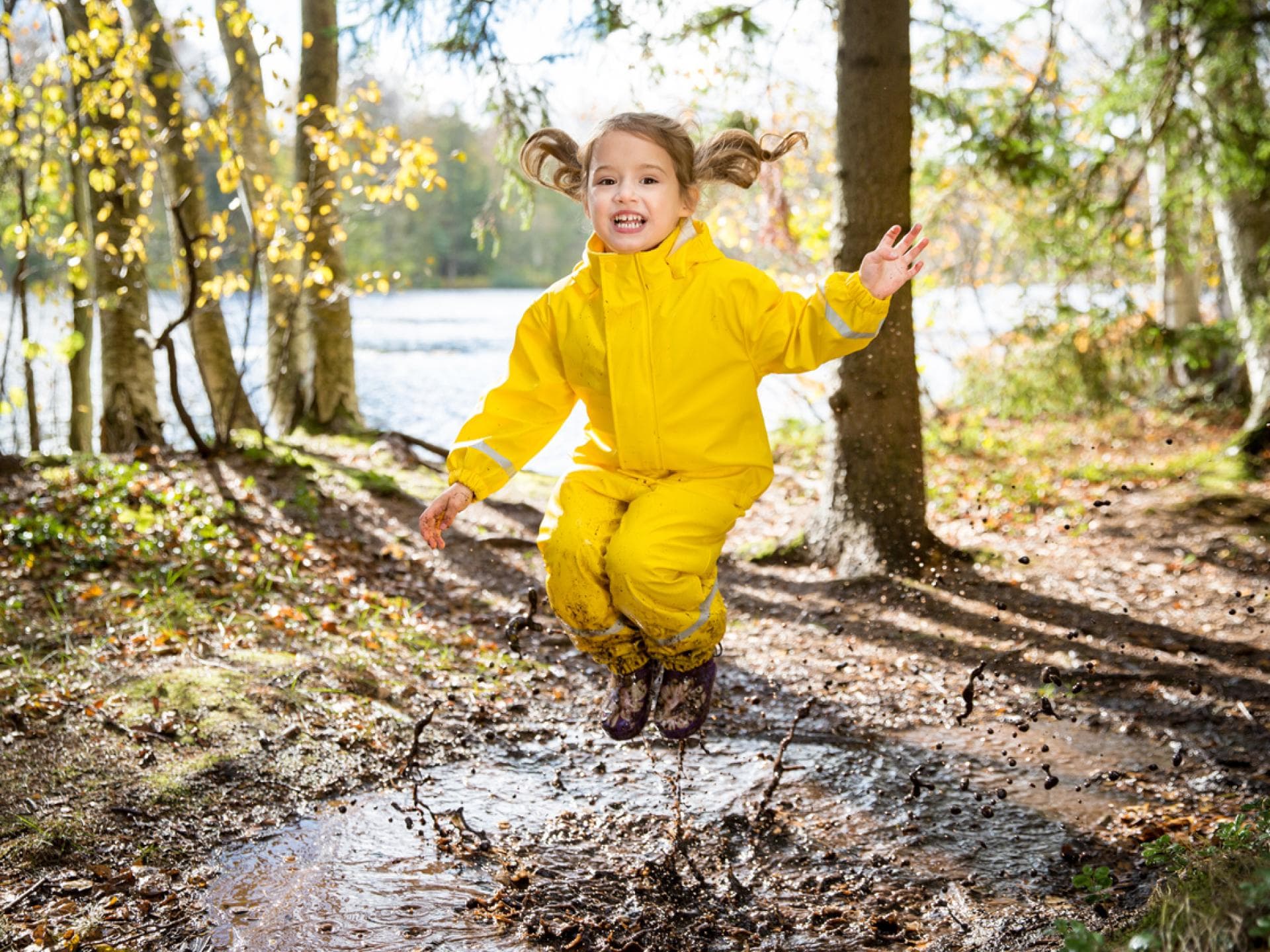 Draußen spielen beeinflusst die Entwicklung von Kindern positiv. Kind spielt draußen und springt in Pfütze