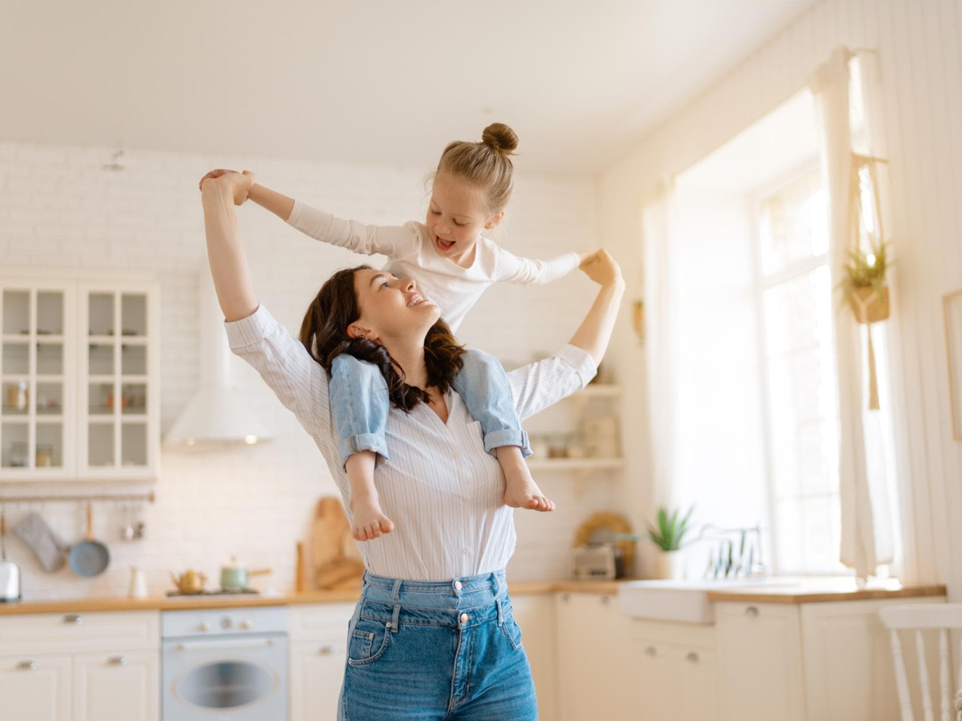 Viele Eltern entscheiden sich heute für neue Erziehungswege. Mutter trägt Tochter in der Küche auf den Schultern.