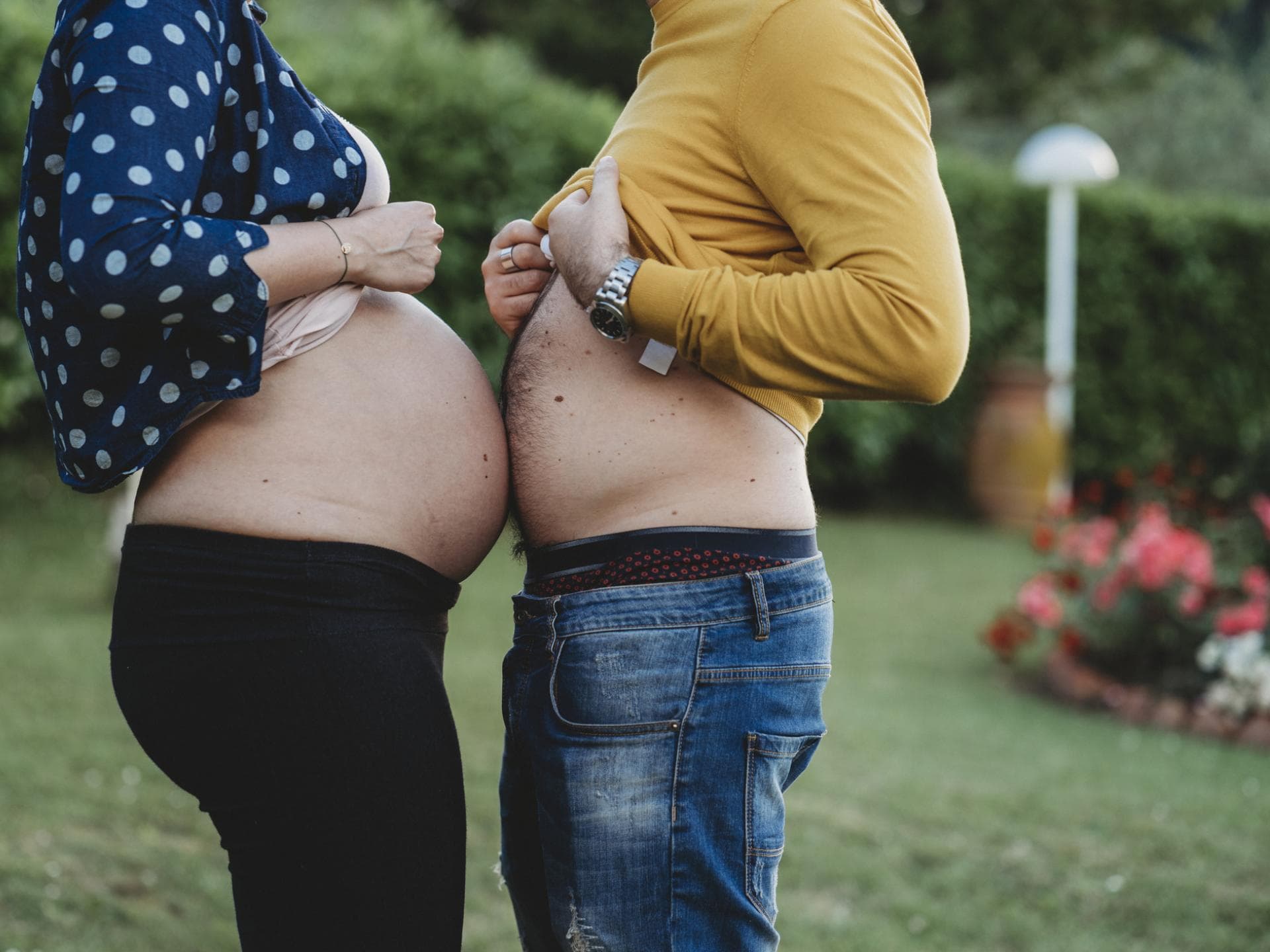 Manchmal wird der Mann in der Schwangerschaft "auch" dick. Schwangere Frau und ihr Mann halten ihre Bäuche aneinander.