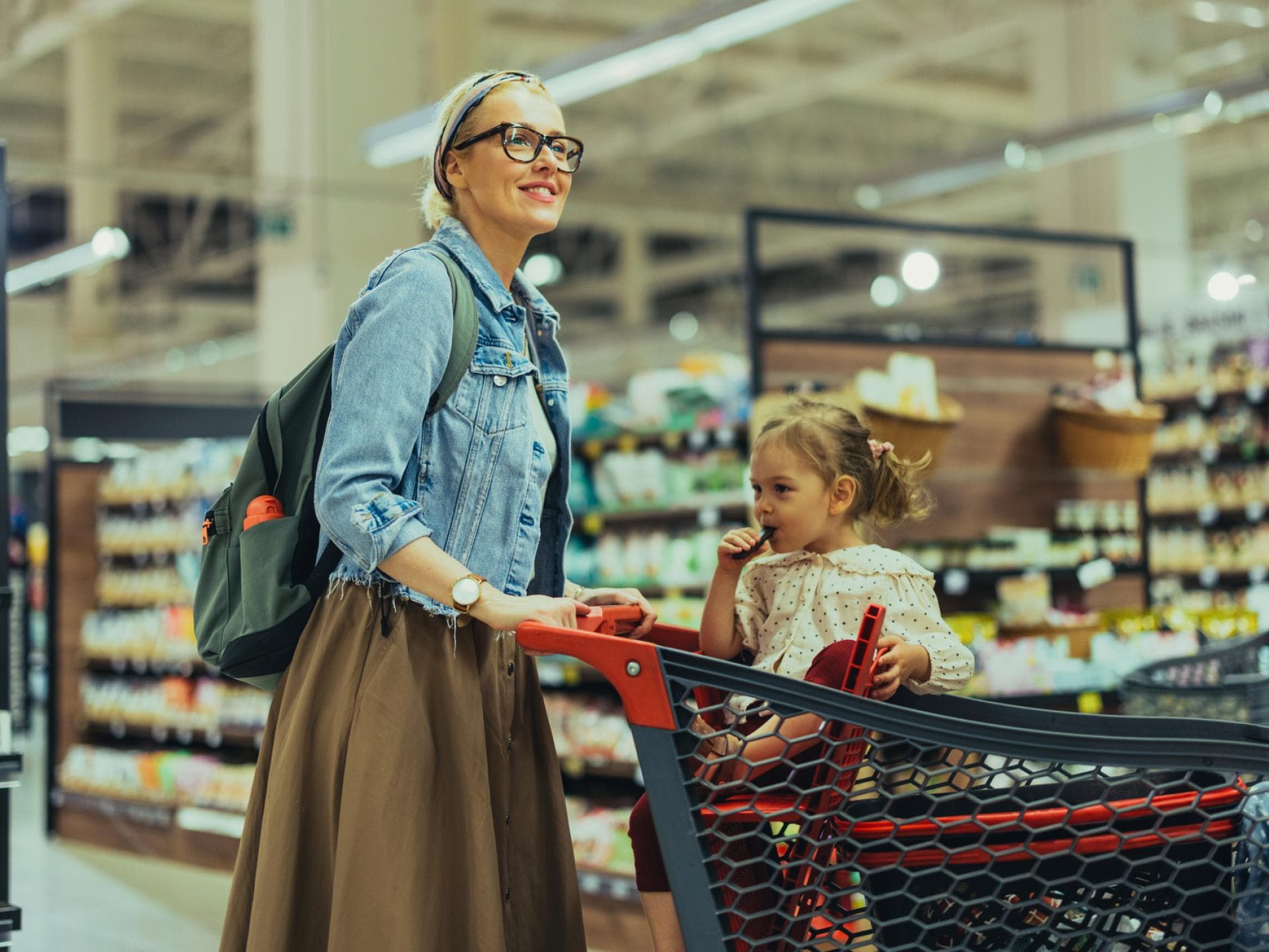 Wenn Kinder unbezahlt im Supermarkt snacken – ist das okay? Eine Mutter schiebt ihre Tochter im Einkaufswagen.