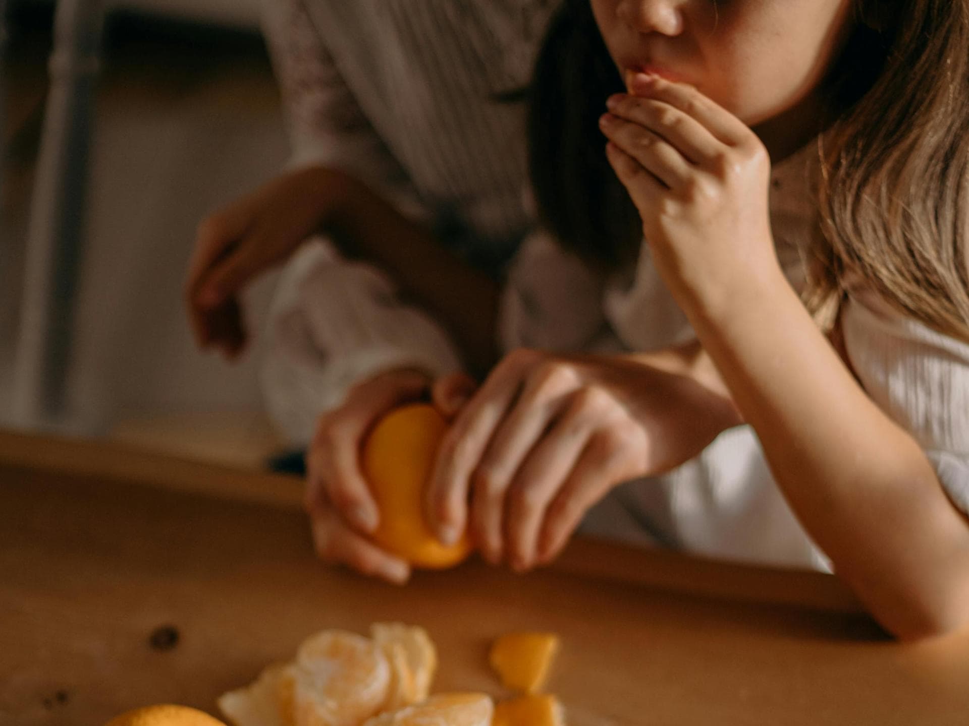 Mandarinen sollte man immer waschen vorm Schälen. Mädchen isst Mandarine, Mutter schält sie.