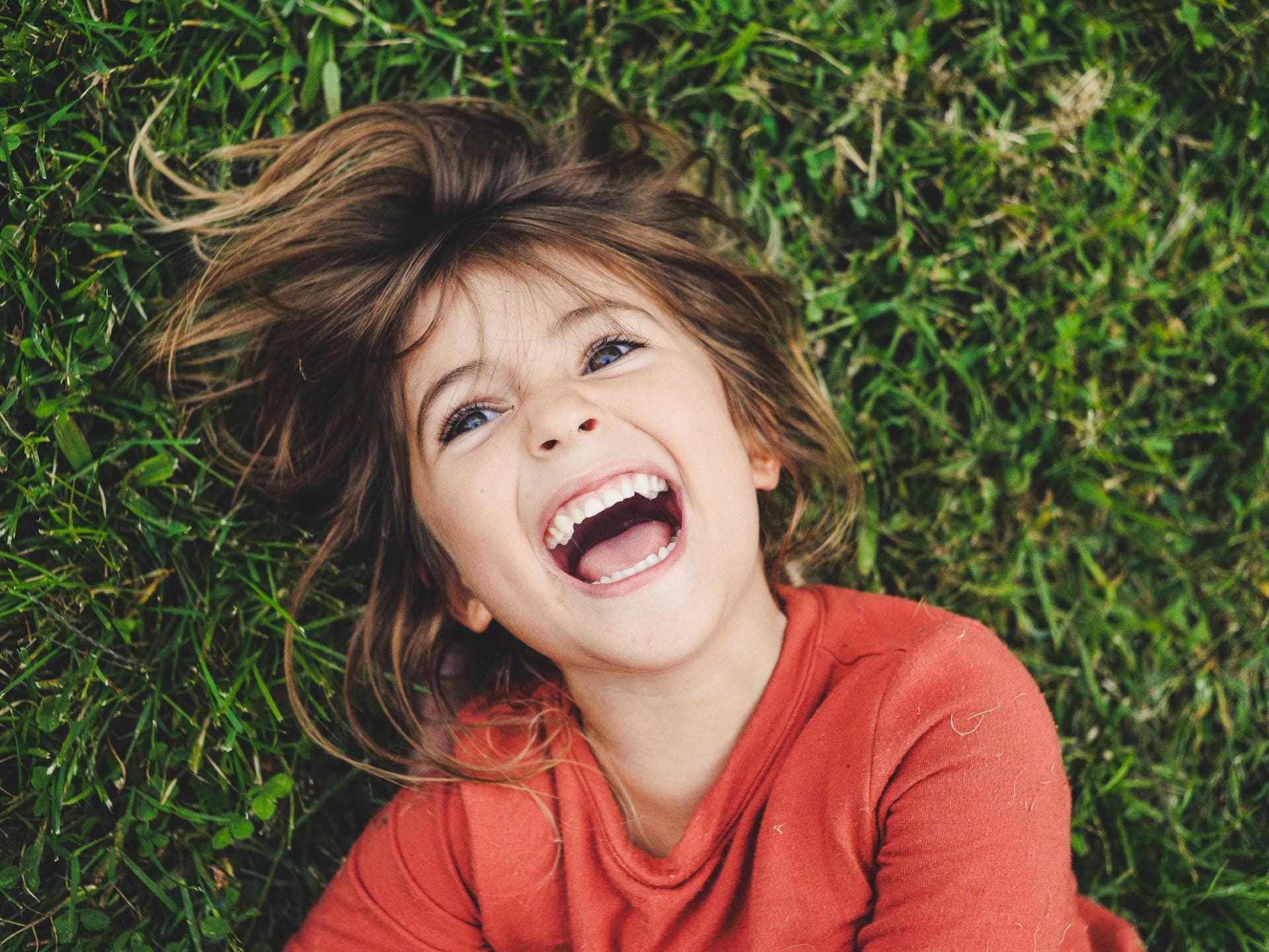 Kinderwitze für jedes Alter. Ein Mädchen, das im Gras liegt und lacht.